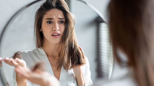 Portrait of stressed young woman with bunch of fallen hair in hand