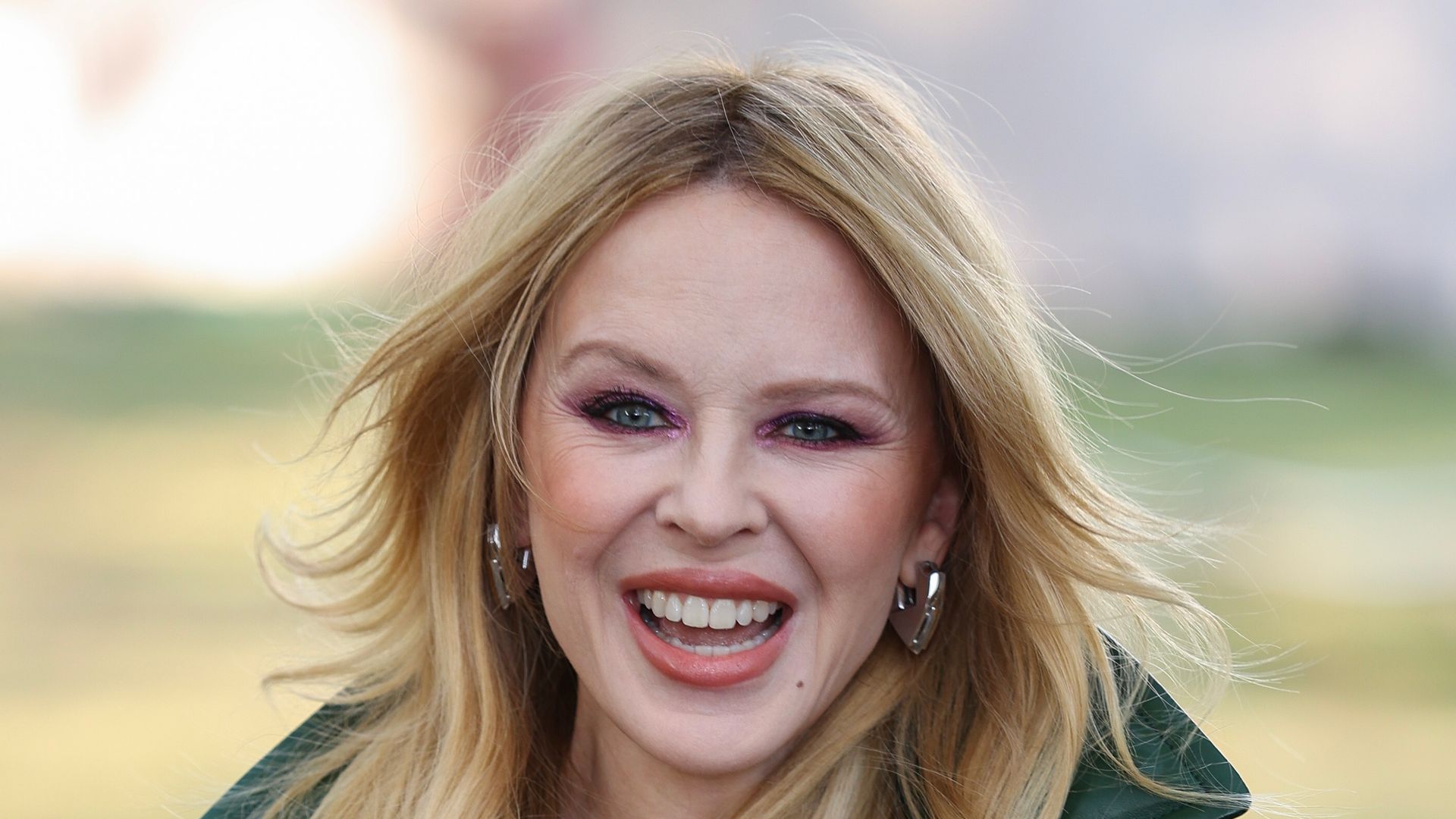 Kylie Minogue smiling in green trench coat 