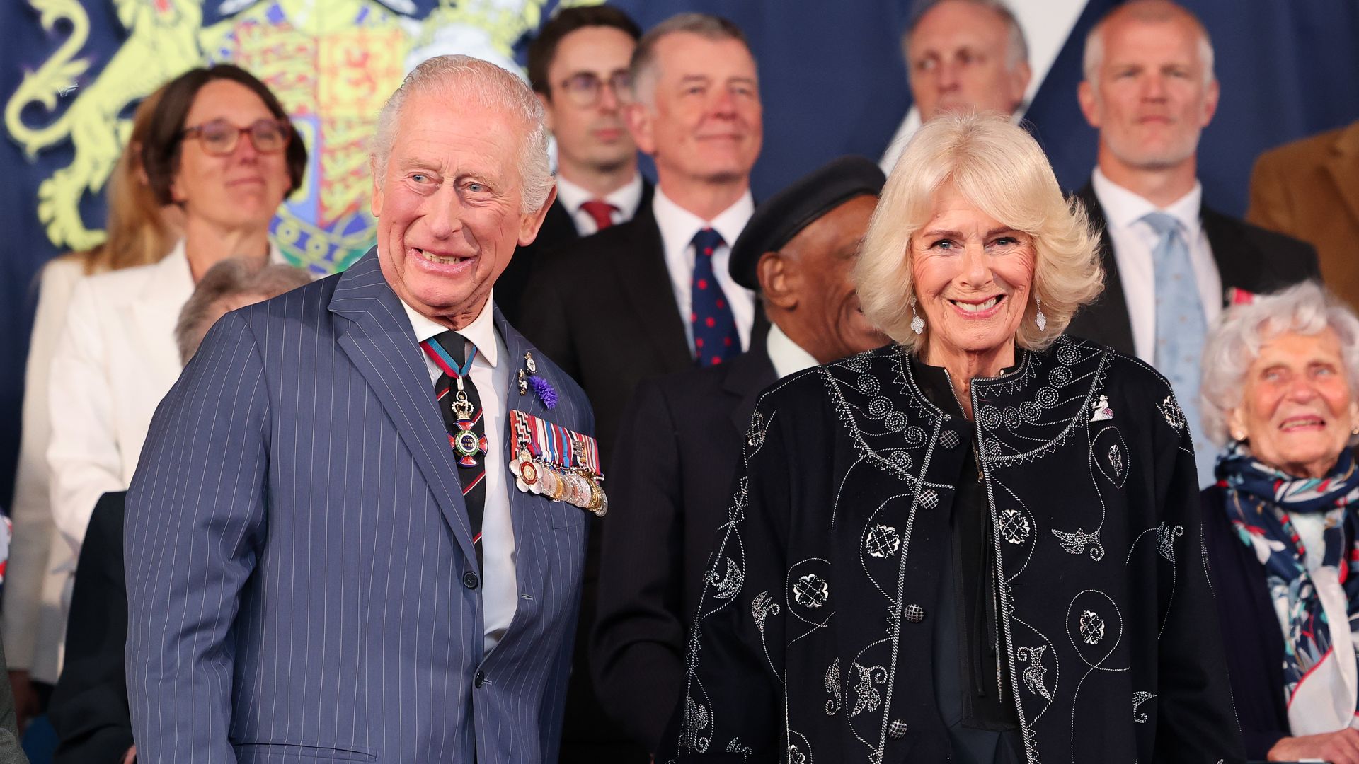 King Charles in a blue suit standing with Queen Camilla in a black outfit