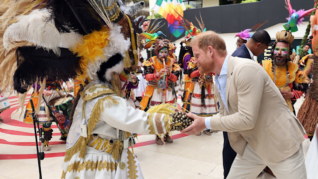 Prince Harry shaking hands with a performer in an extravagant costume