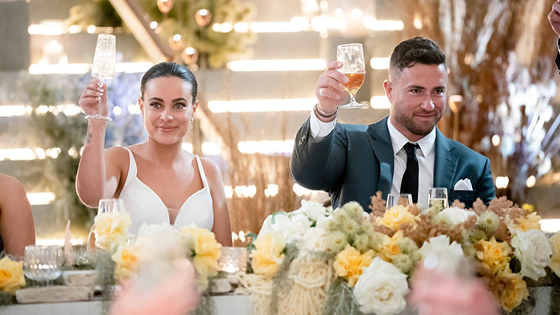 Bronte and Harrison hold up glasses in toast on wedding day