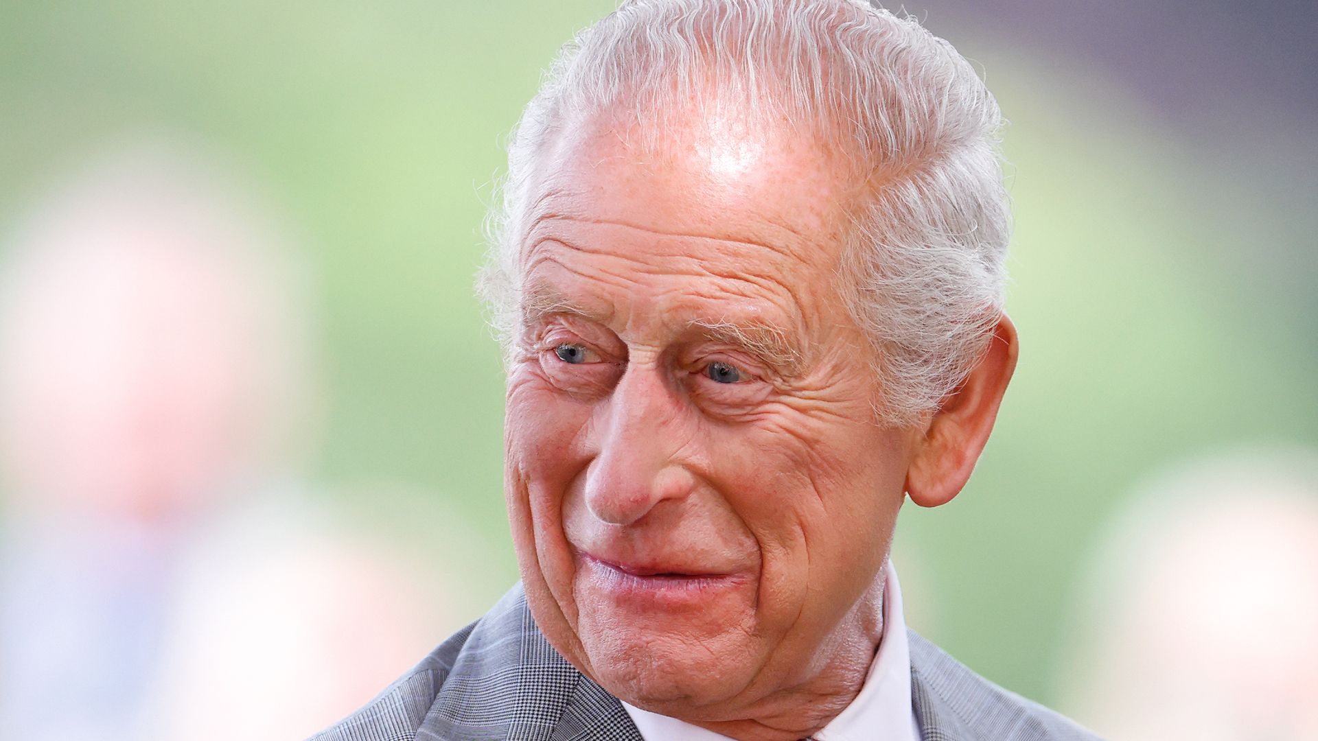 King Charles smiling over shoulder in grey suit