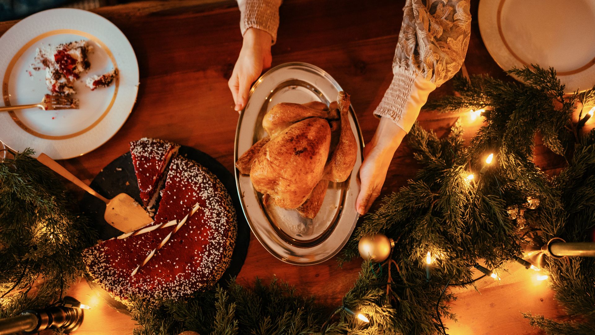 A woman serves roasted duck at a festive, warmly lit Christmas dinner table.