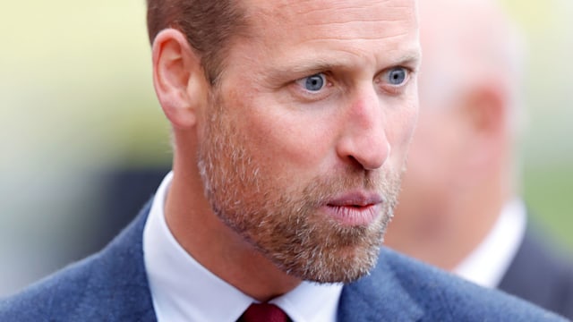 Prince William looking shocked and pursing his lips in a blue suit