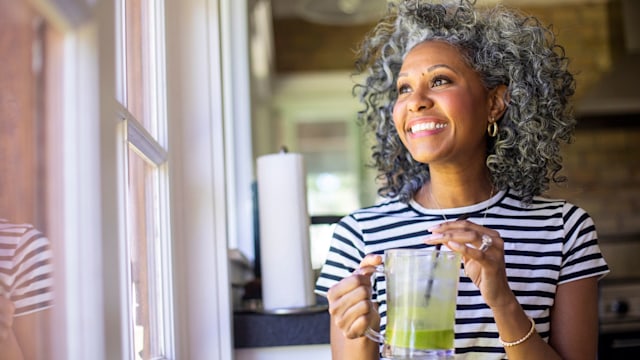 A beautiful black woman with white curly hair  drinks coffee in her kitchen