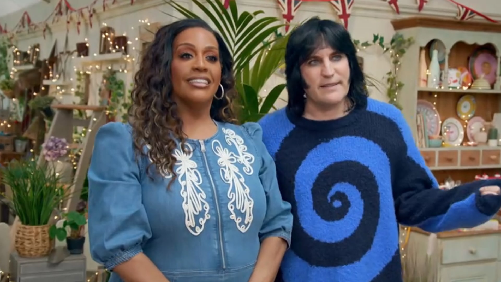 two presenters standing in front of cabinet of plates and fairy lights