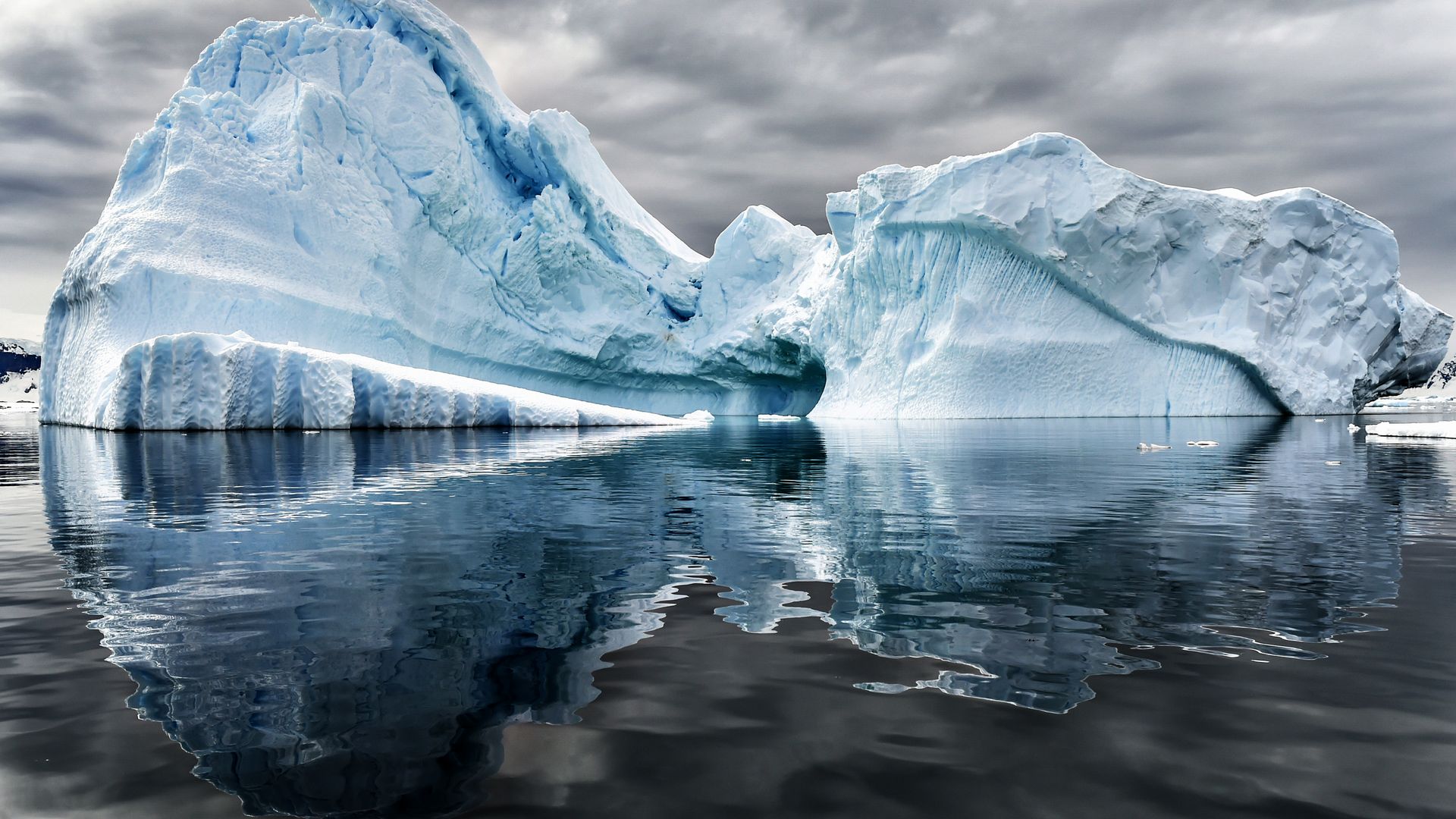 A big iceberg in the middle of the ocean with grey clouds in the sky