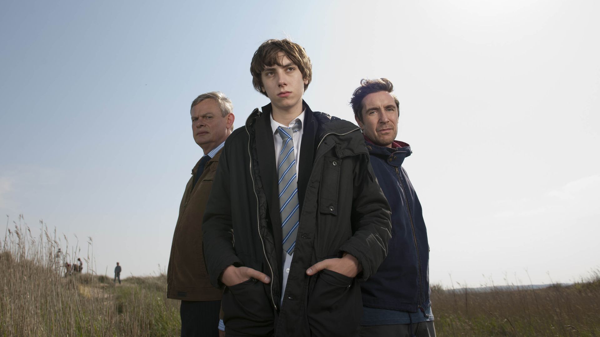 teenage boy standing in front of two men in field