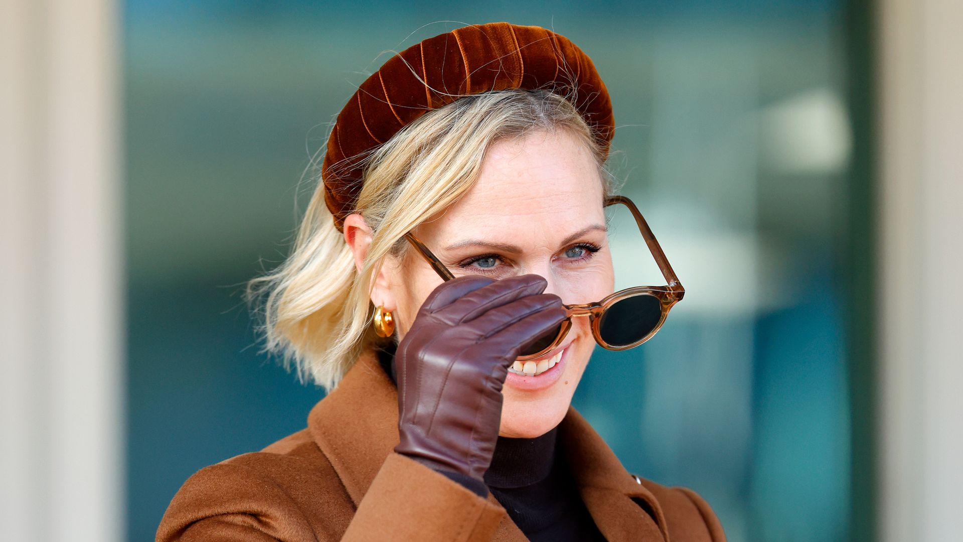 Zara Tindall taking sunglasses off her face in brown coat