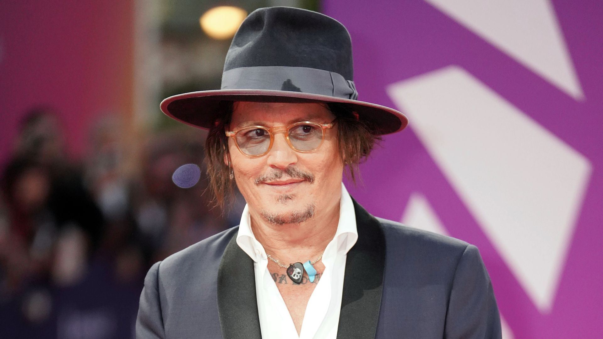 Johnny Depp smiling on a red carpet and looking to the right, he is wearing a hat