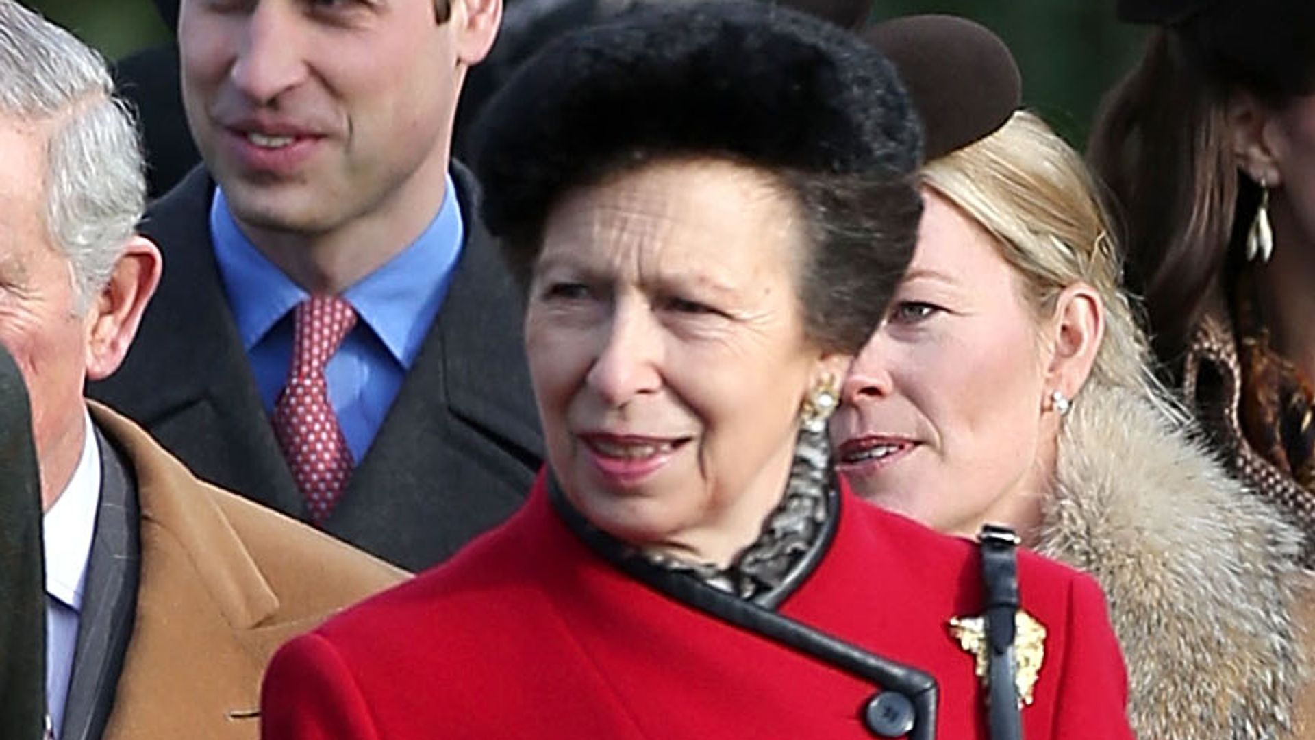 Princess Anne in a red coat outside with the royal family