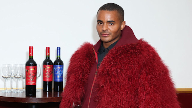 Layton Williams posing in red fur coat holding wine