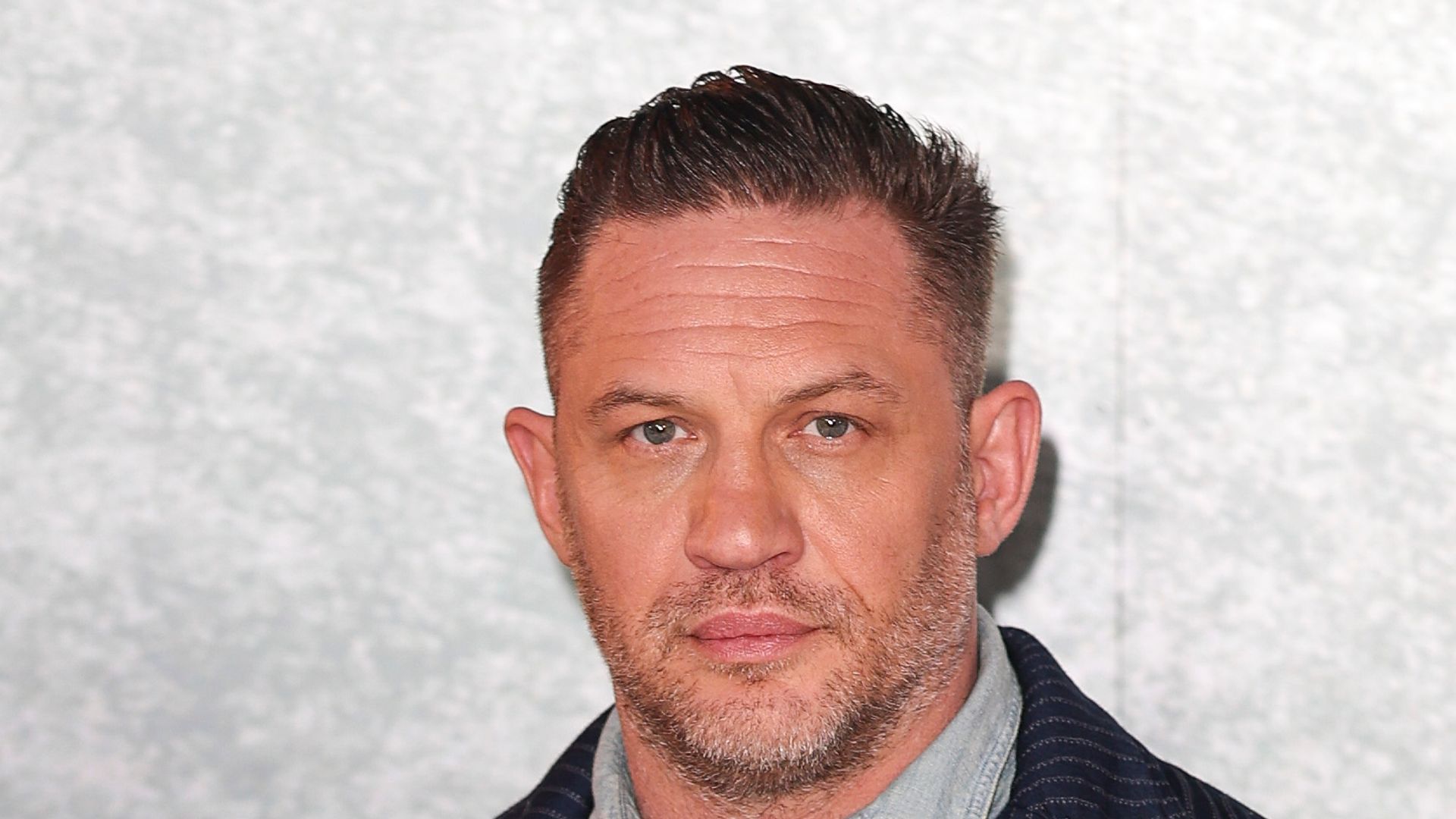 Tom Hardy posed in suit with grey backdrop