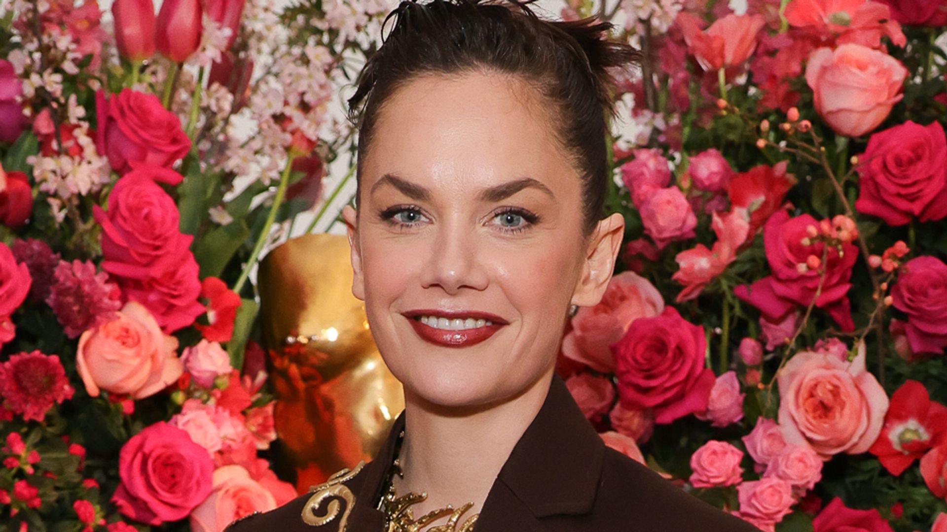 Ruth Wilson in a black suit against the backdrop of pink roses