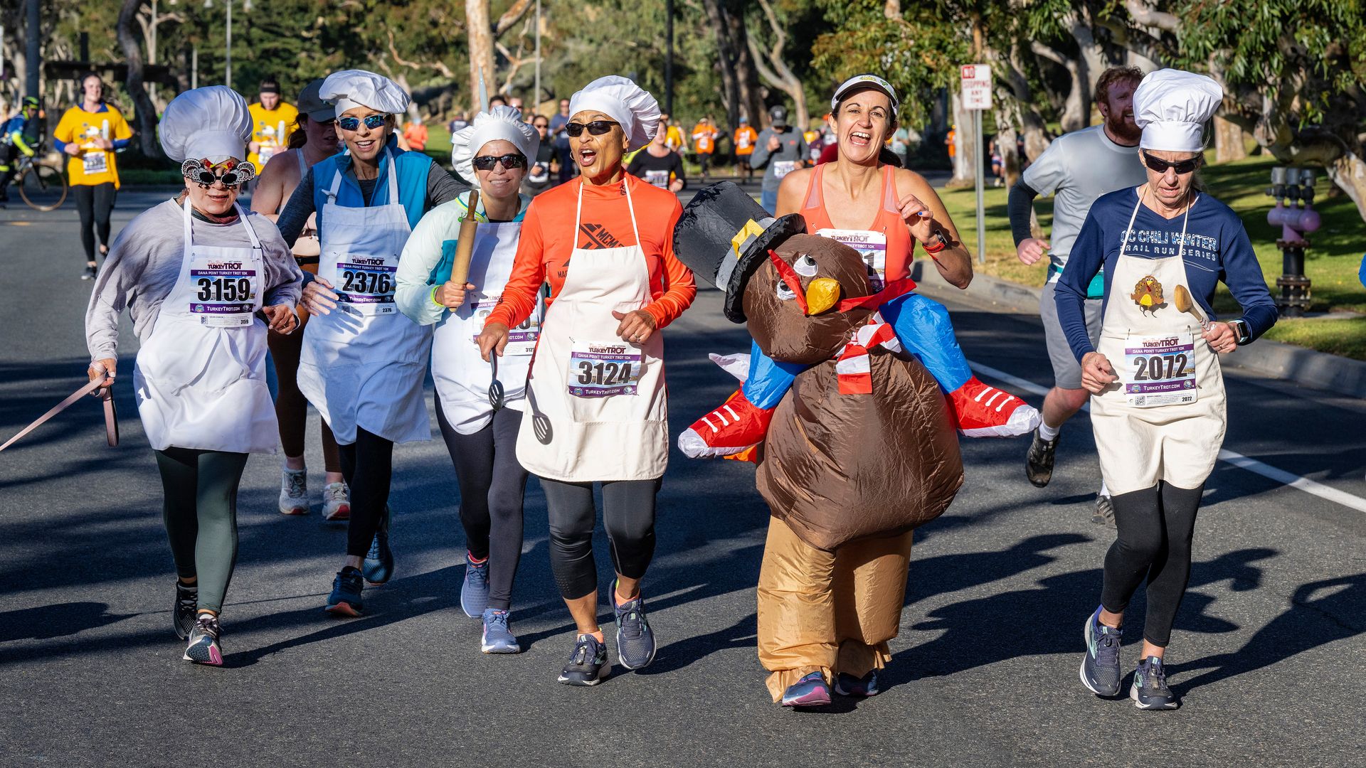 A runner dressed as a turkey is chased by chefs as they near the finish line during a Trot