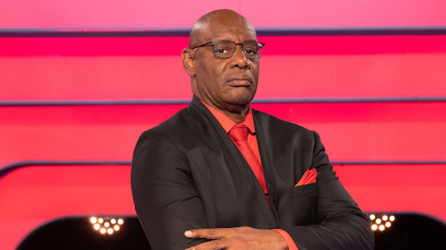 Man in black suit standing in tv studio with arms folded