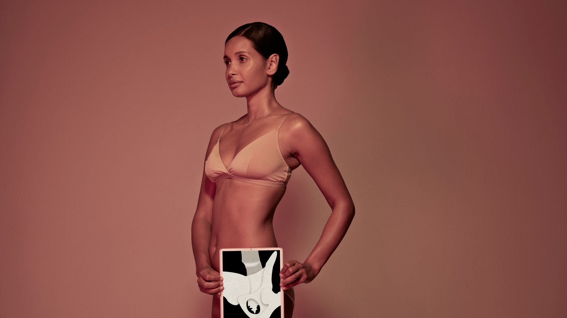 Female holding tablet in front of body to display coloured x-ray illustrations made out of hand made paper structures