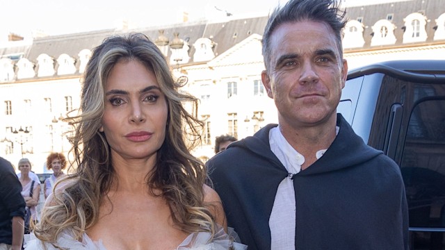 Ayda Field in a white feathered dress and Robbie Williams in a cape at Paris Fashion Week in 2022