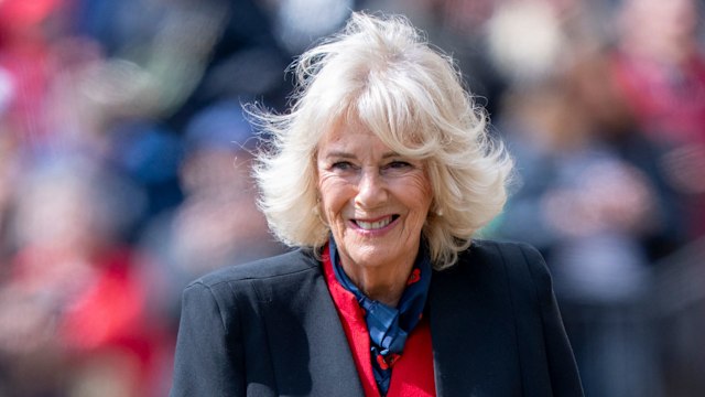 Queen Camilla in red dress and black cape smiling