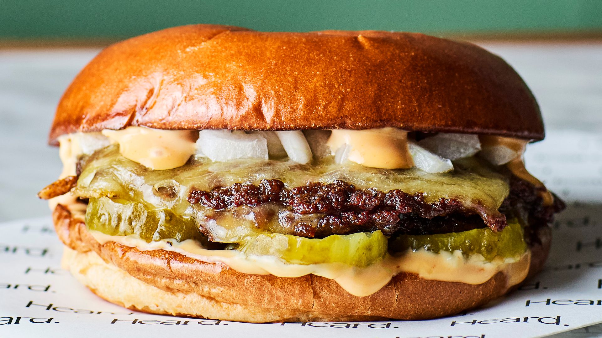A burger with onions, melted cheese, pickles and two patties