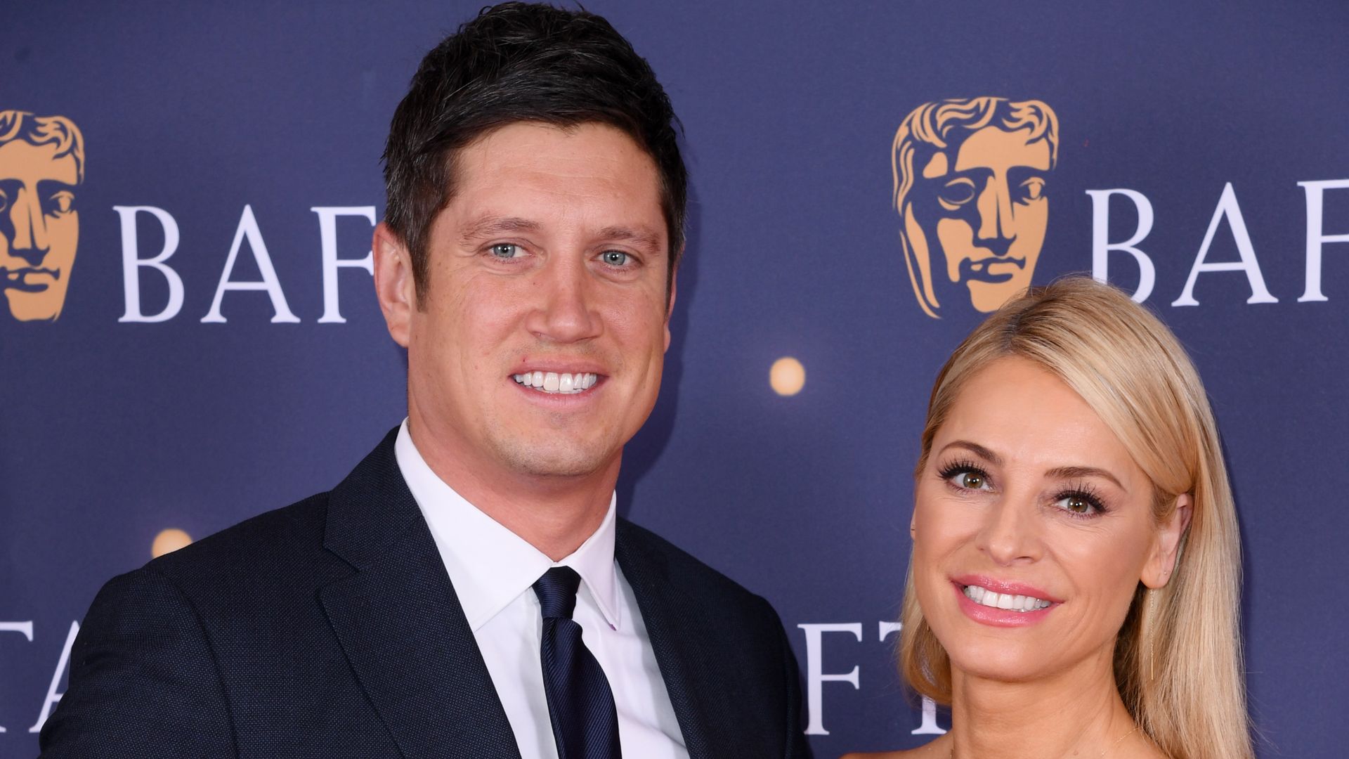 Vernon Kay in suit standing with Tess Daly in red dress