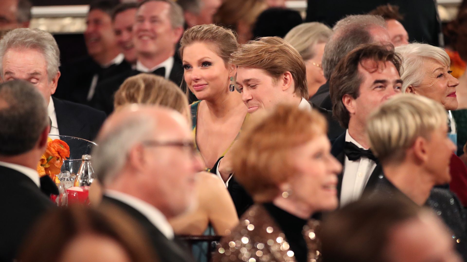 A crowd of faces sat watching an awards ceremony, Joe and Taylor in the mid-distance in focus, smiling