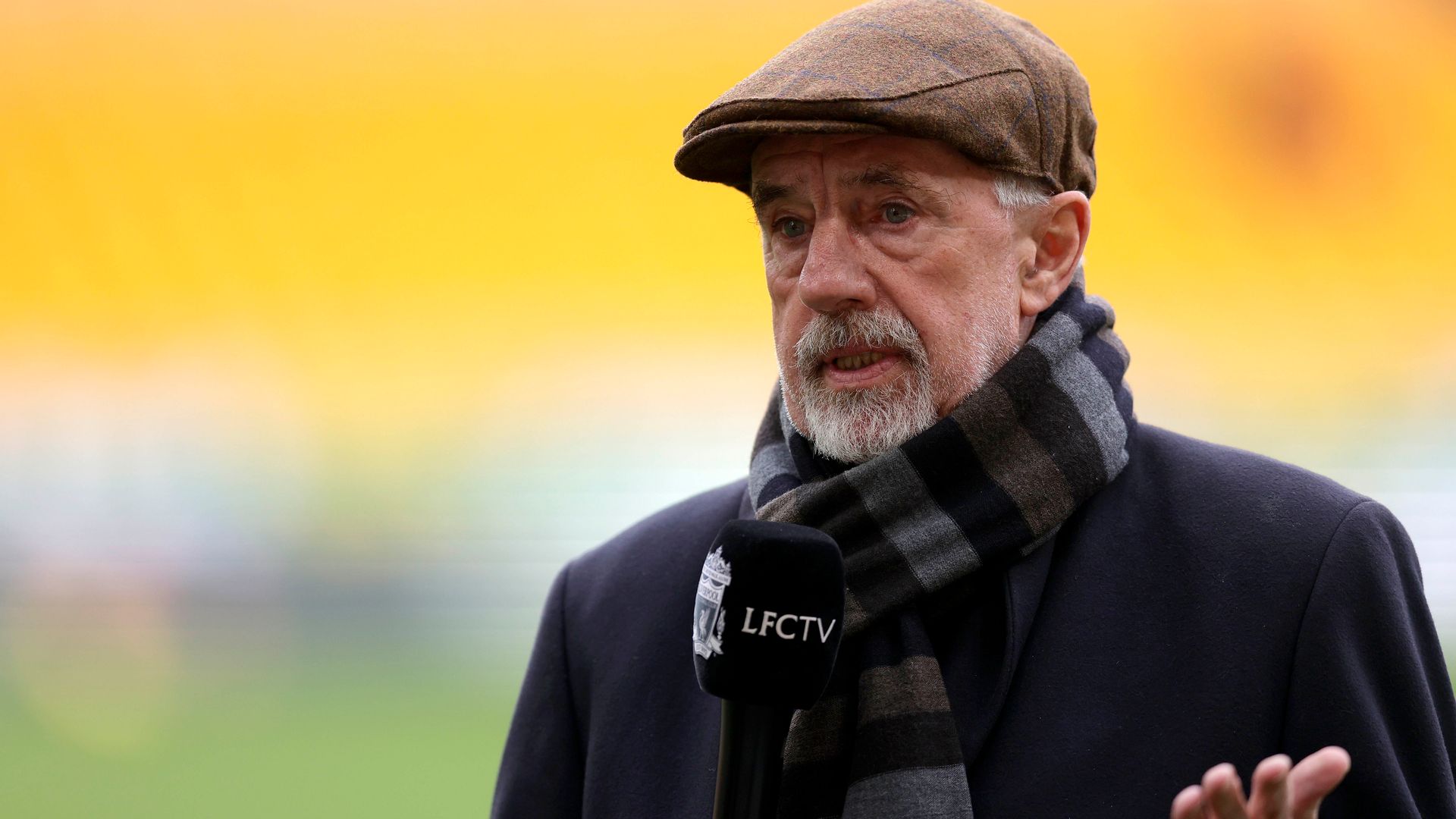 sports pundit in coat, flat cap and striped scarf