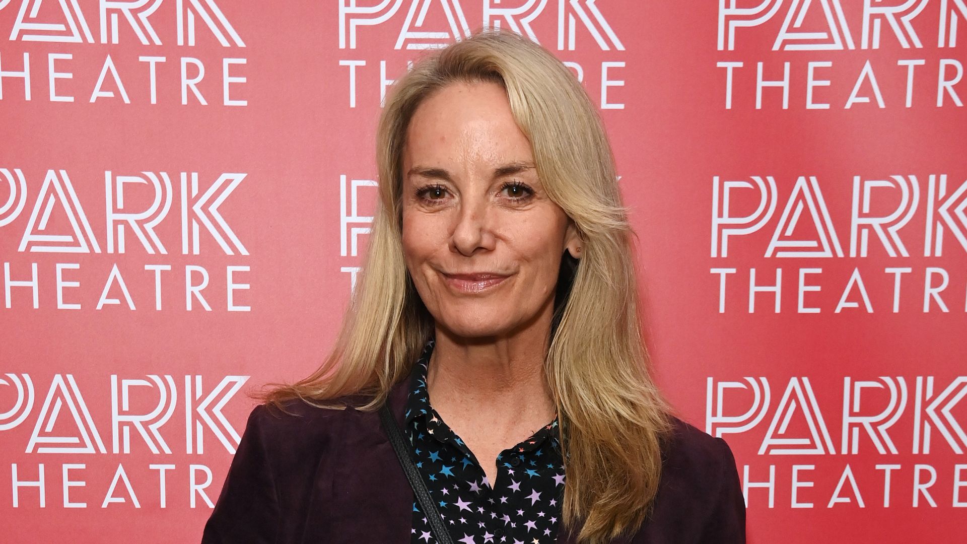 Tamzin Outhwaite in a star print top and black jacket in front of a red background