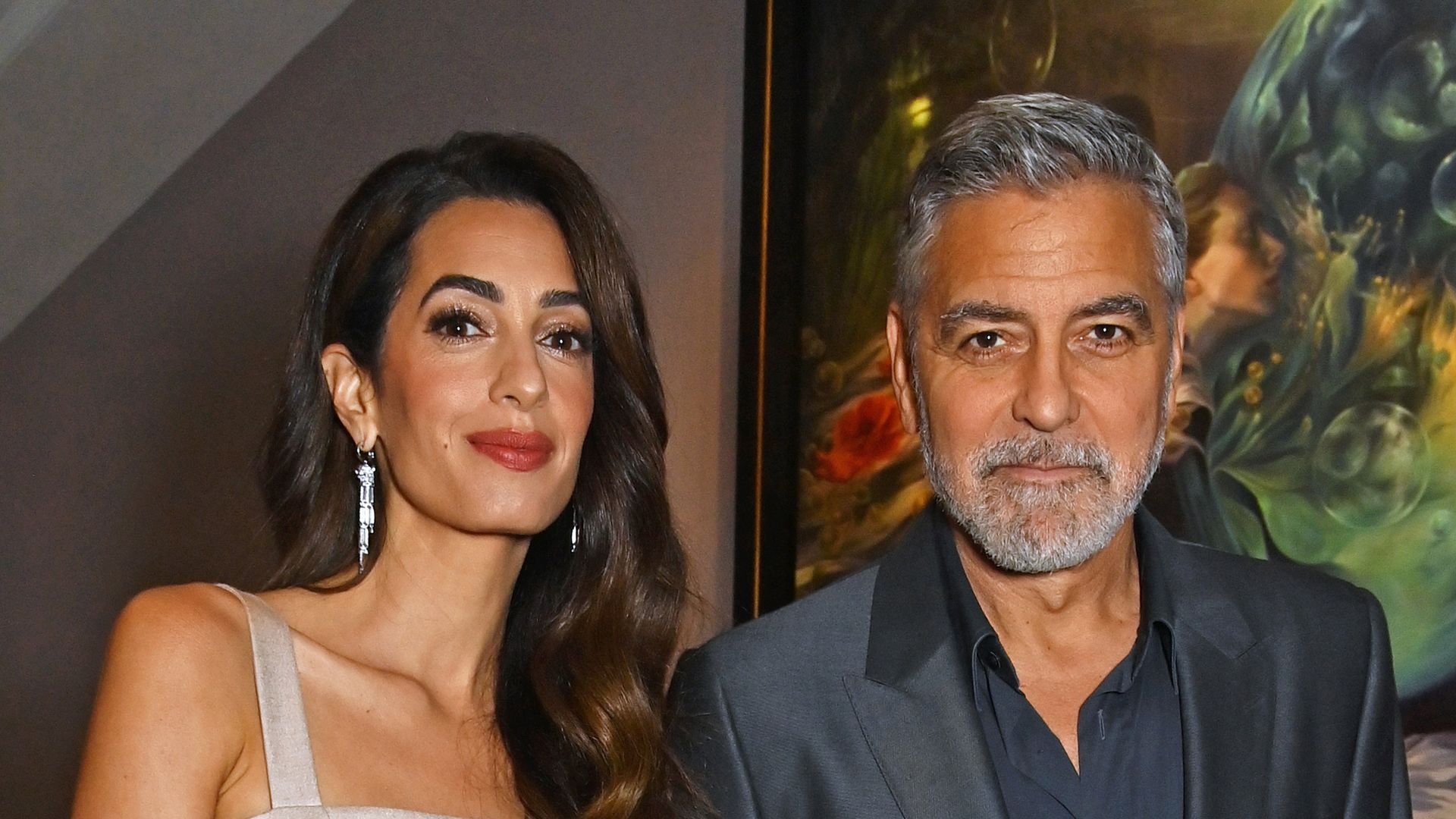 Amal Clooney and George Clooney hold hands while smiling for photographer at event in London