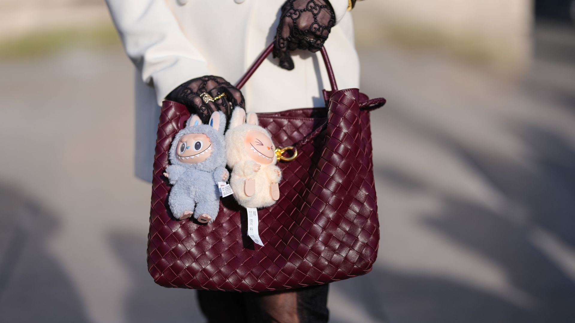best bag charms - photo is of a street style fashion star carrying a bottega bag with two labubu bag charms attached