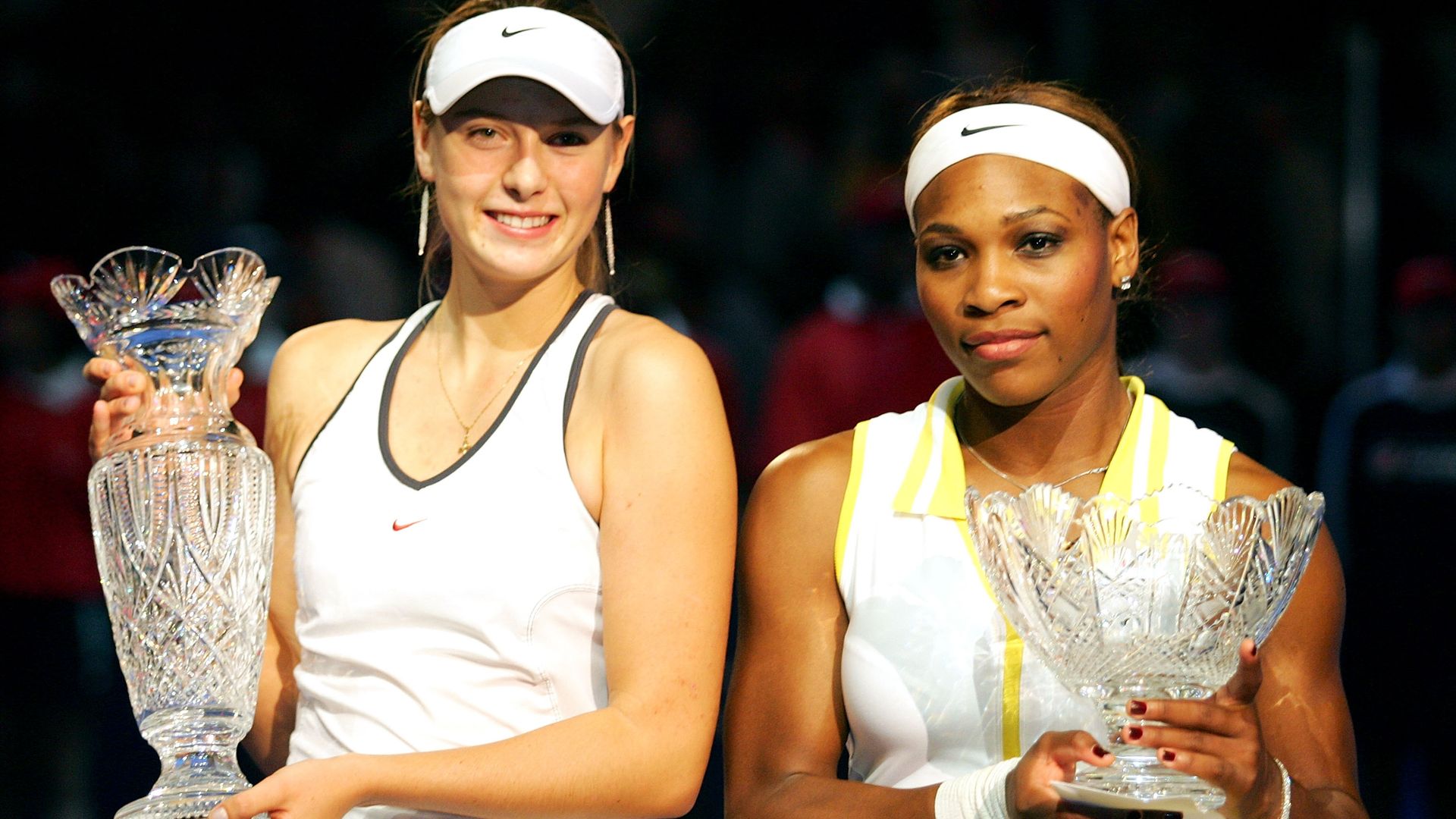 Two tennis players stand together holding trophies