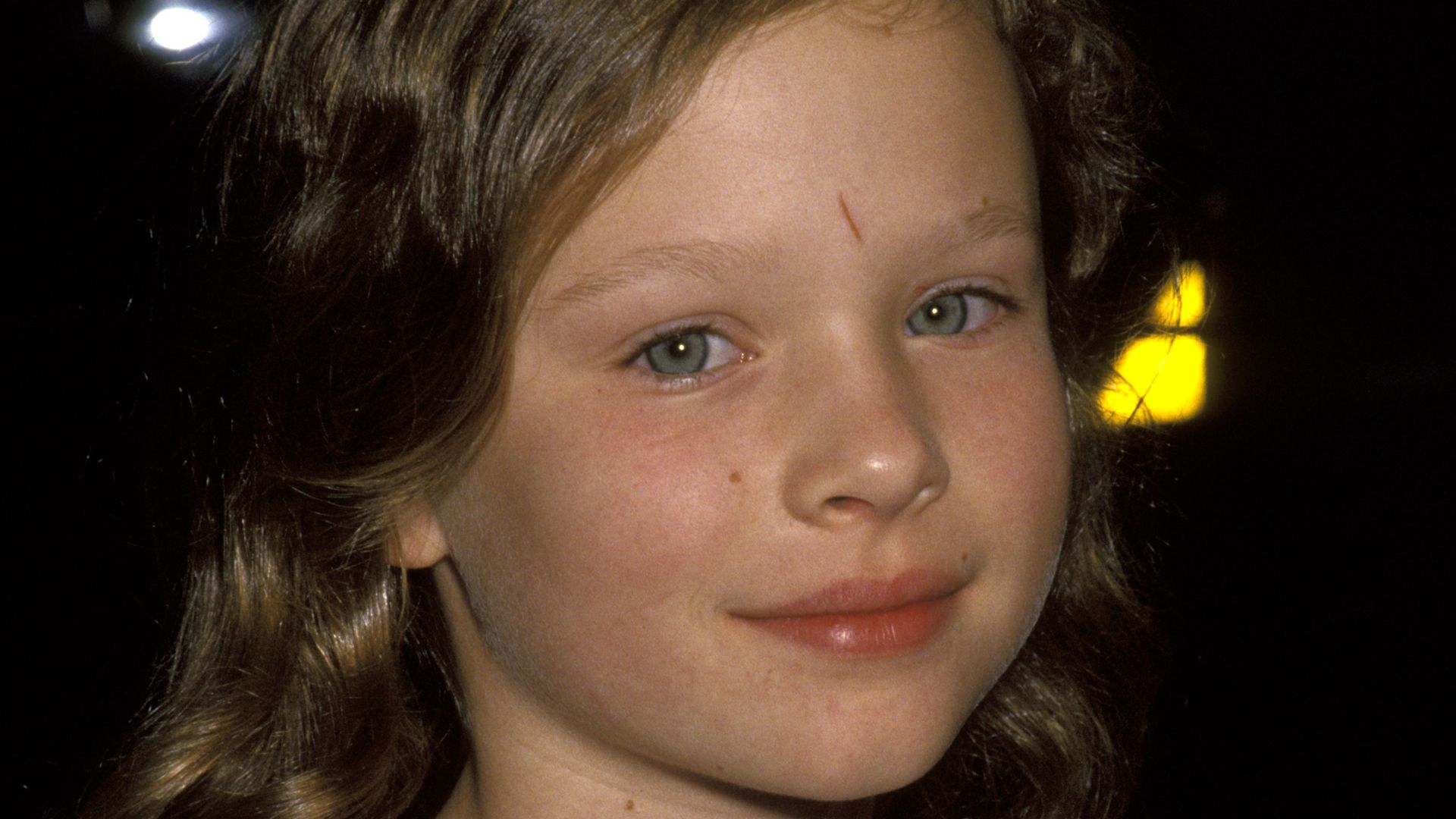 Thora Birch as a child in a white top smiling for the camera shyly