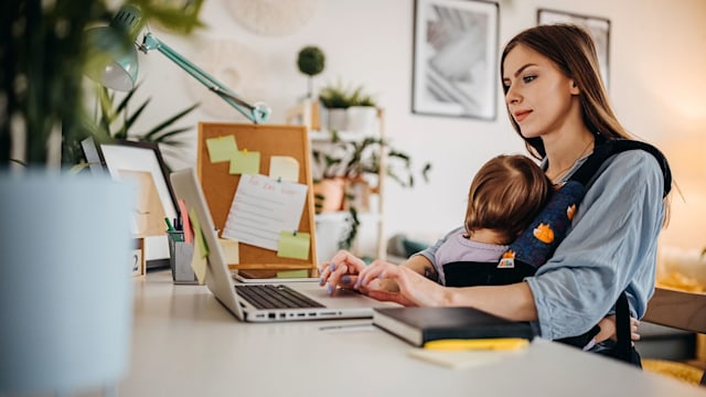 Business mother working from home and holding baby in arms