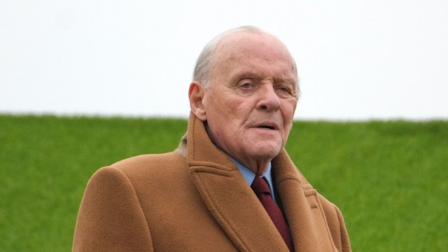 anthony hopkins in beige coat standing on grassy hill