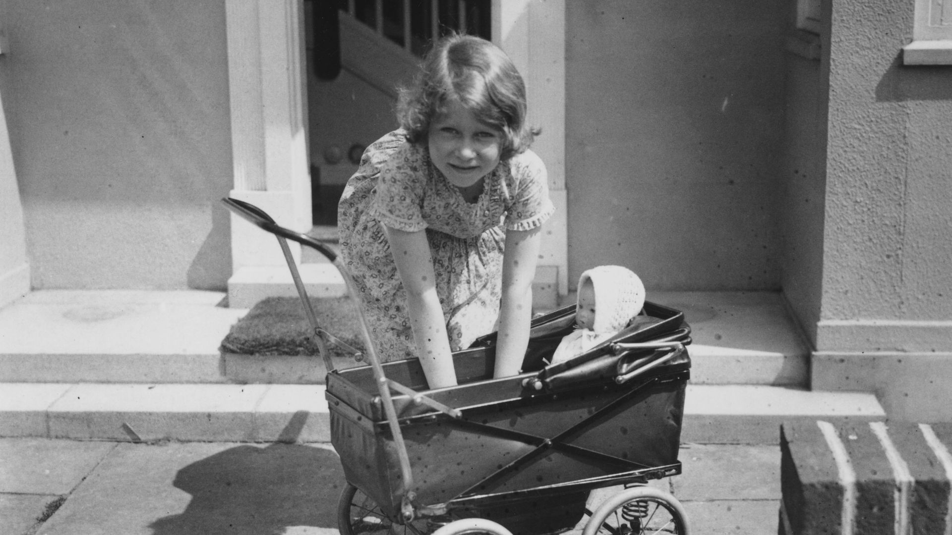 A young Queen Elizabeth playing with a baby doll and a pram