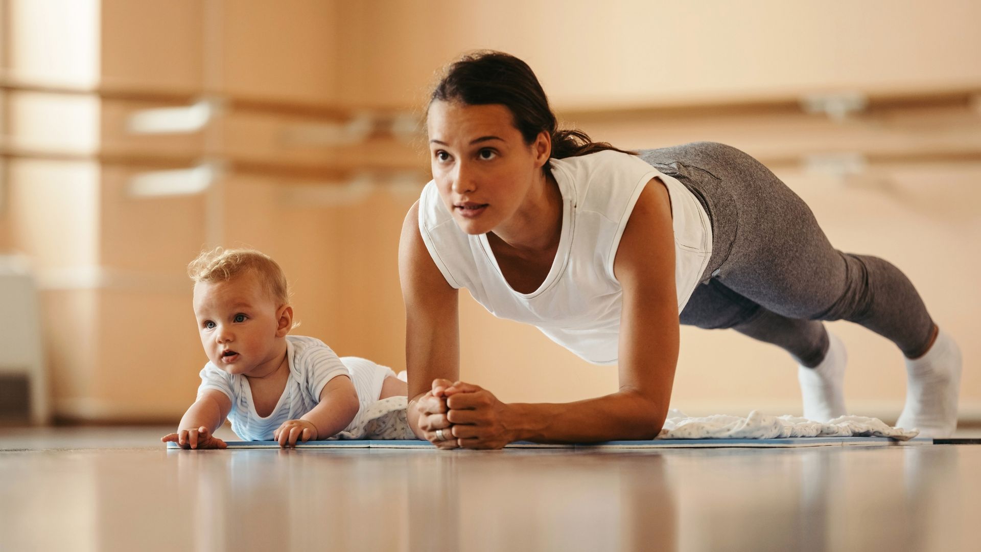 Mother exercising in plank position next to her baby in a health club