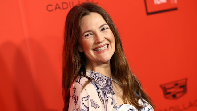 Drew Barrymore smiling in a printed dress on a red background