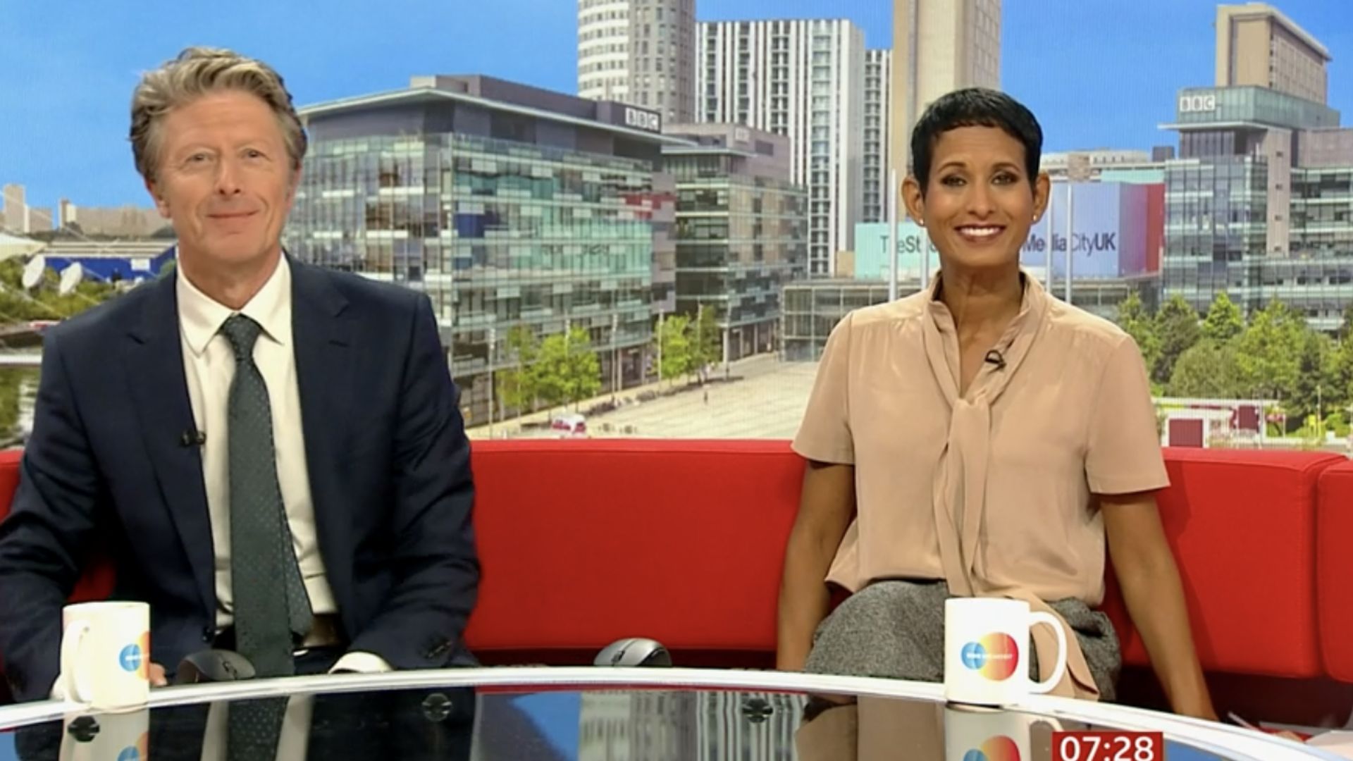 Naga Munchetty and Charlie Stayt smiling on the red couch with breakfast bbc