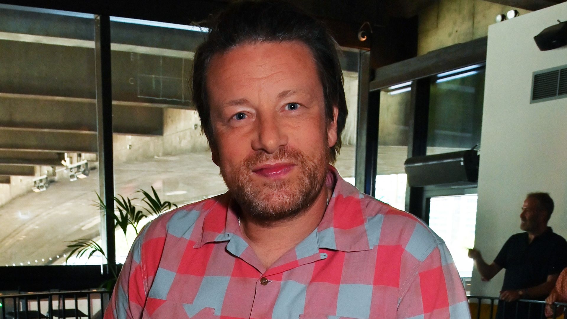 Jamie Oliver posing for a photo in a white an pink checked shirt at an event
