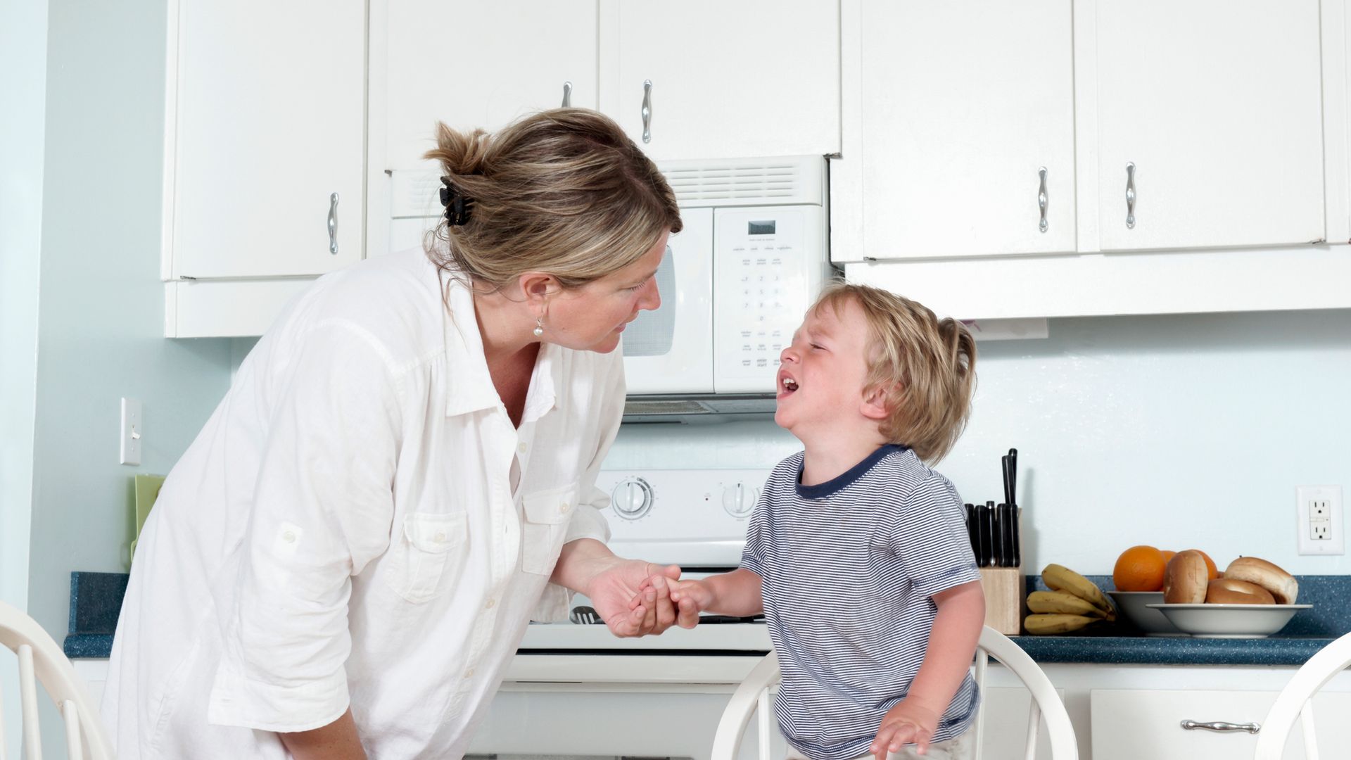 A mother trying to calm her crying toddler at home in their kitchen.  