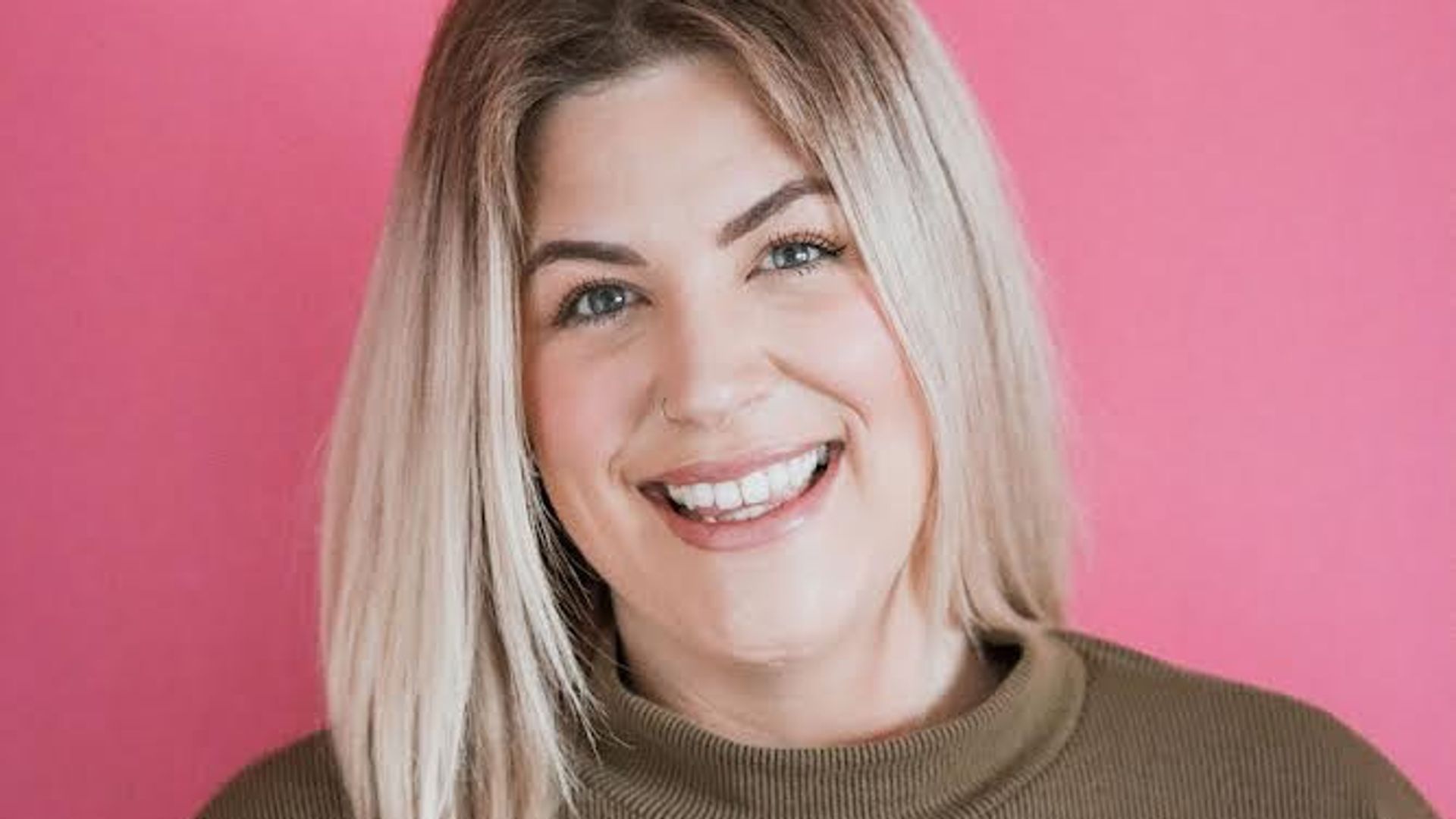 Smiling blonde woman in cosy jumper on pink background 