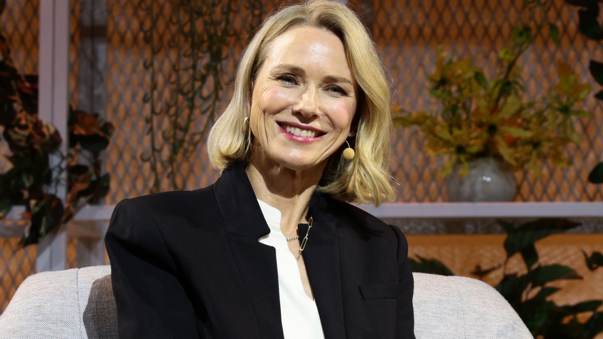 Naomi Watts smiling while sat on stage for an interview
