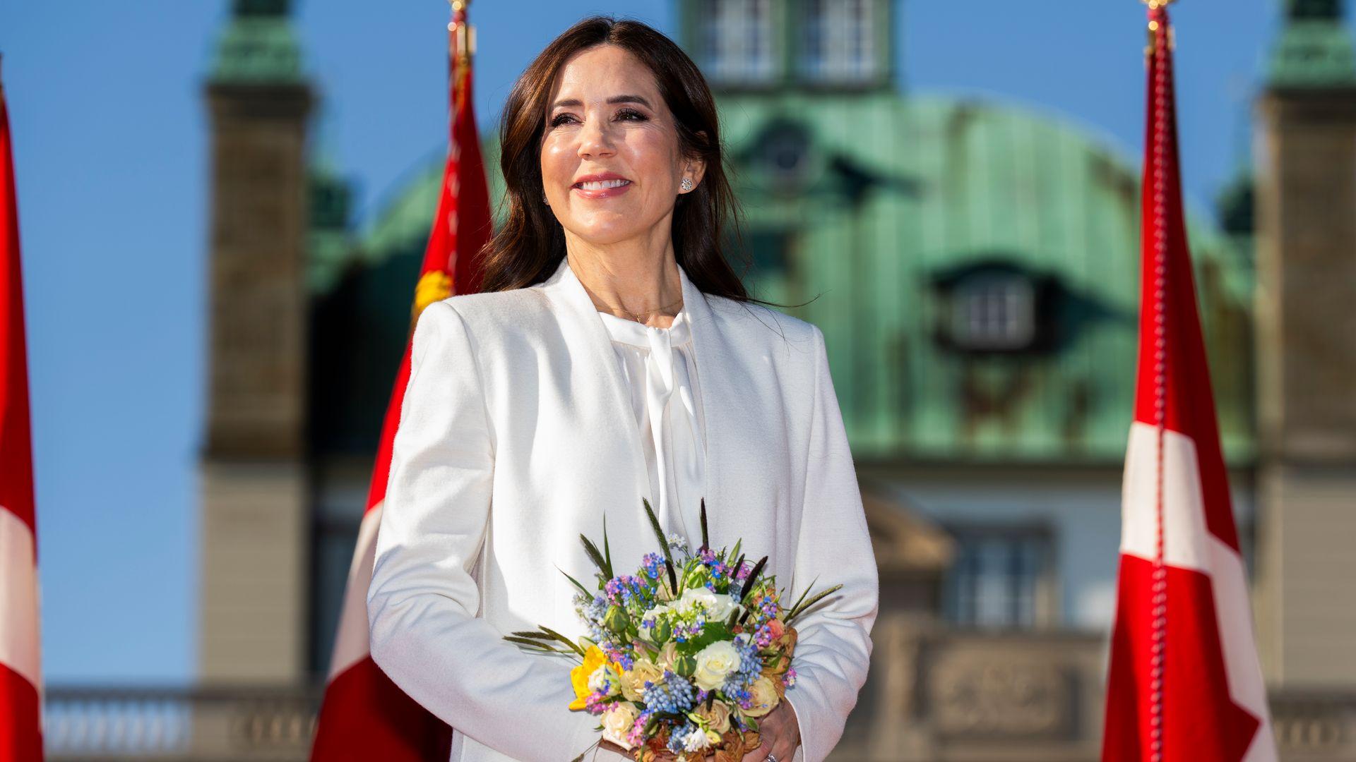 Queen Mary holding flowers in front of Danish flag