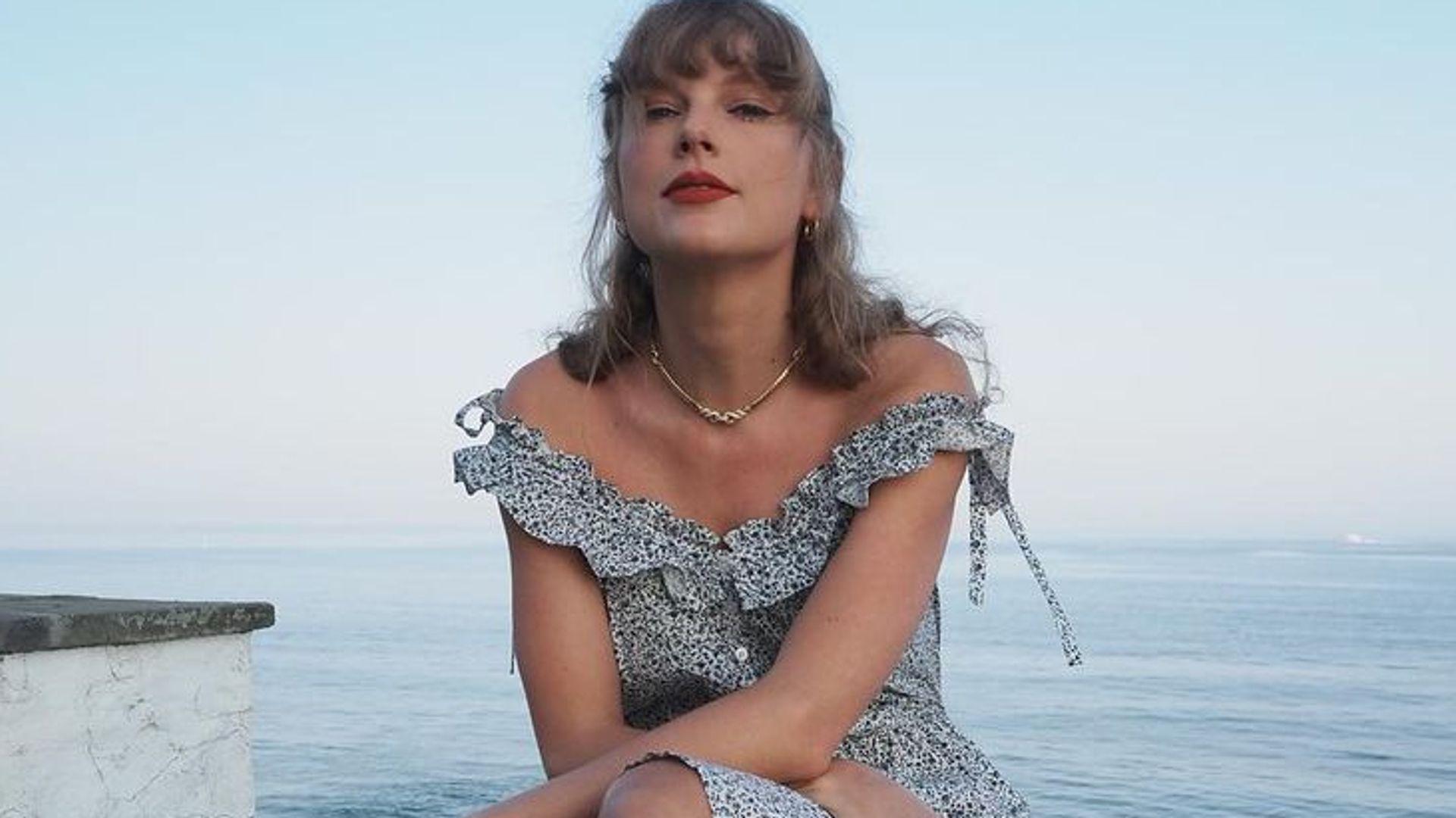 Taylor Swift sits on wall with sea behind her
