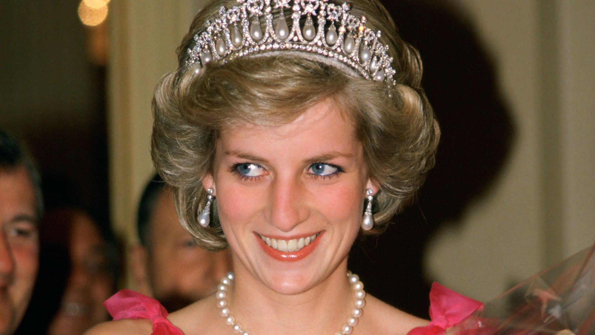The late Princess Of Wales in a pink dress and tiara holding a bunch of roses