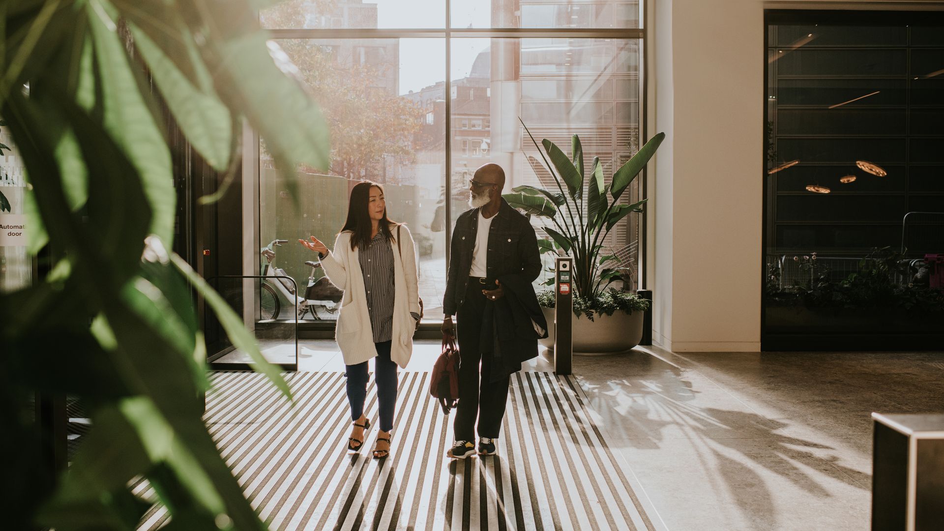 A man and woman enter a large, light filled interior space through rotating doors. It could be a commercial building or a hotel or luxury apartments. They look around in awe.