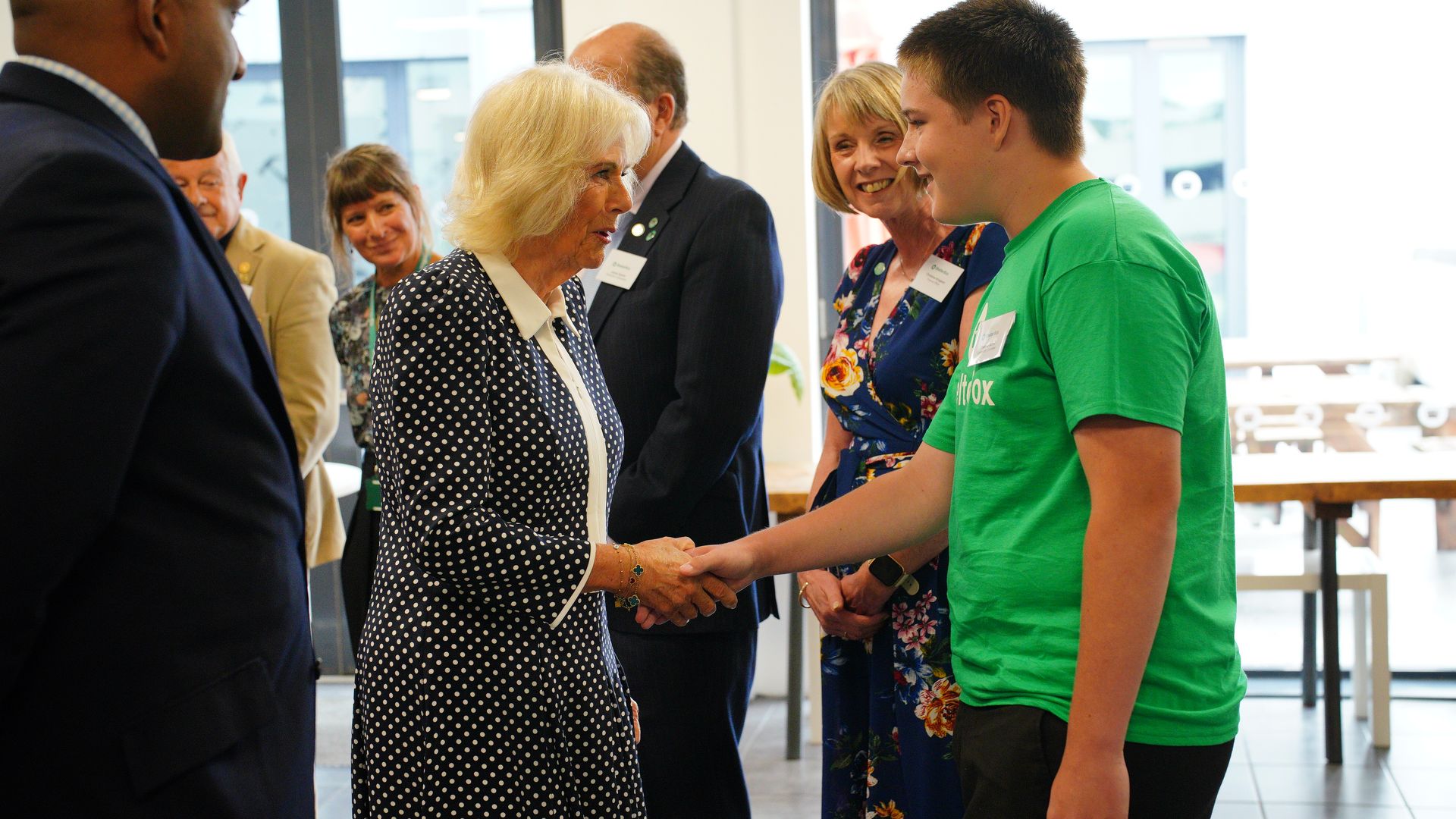 Queen Camilla shaking hands with a boy in a green shirt