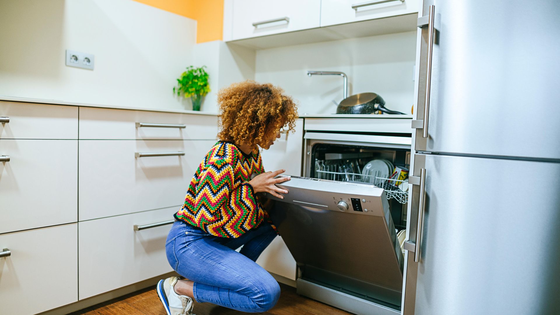Young woman with curly opening the dishwasher in kitchen