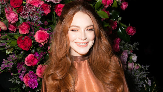 Lindsay Lohan smiling wide with flowers behind her