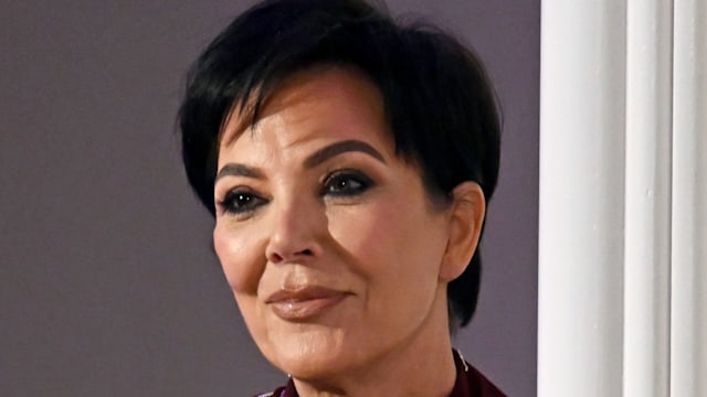 Kris Jenner looking serious in a burgundy shirt dress